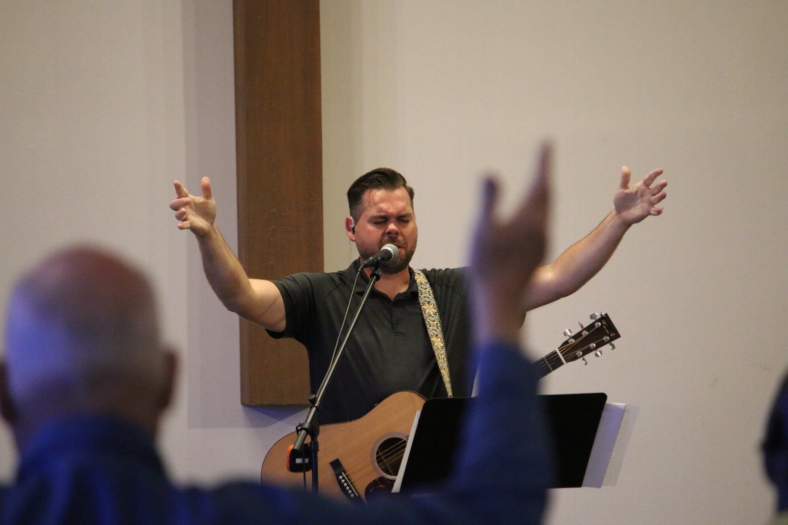 The worship leader sings with arms open wide on stage