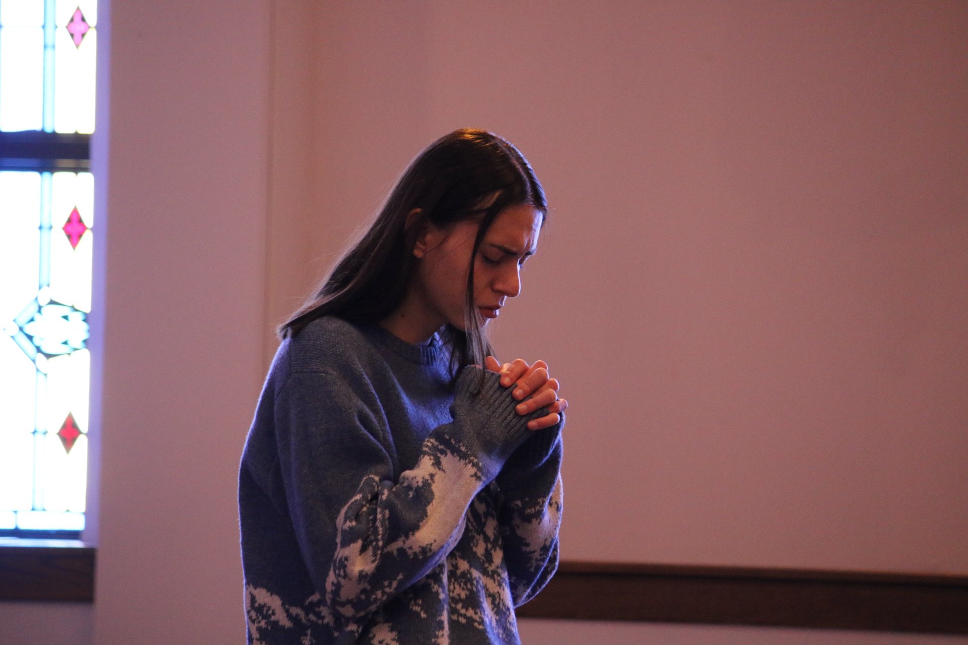 A young woman prays quietly with folded hands in the sanctuary